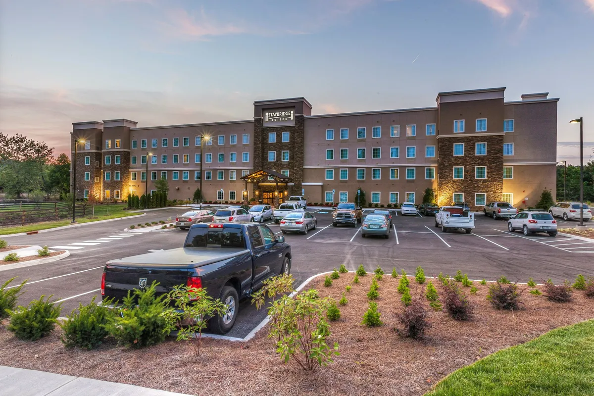 This image shows the hotel's main entrance surrounded by landscaped gardens and a spacious parking lot. The view is bathed in warm sunset light, emphasizing the inviting and welcoming atmosphere offered to guests. The entrance is clearly visible, showcasing easy access to the property after a day of exploring nearby attractions.