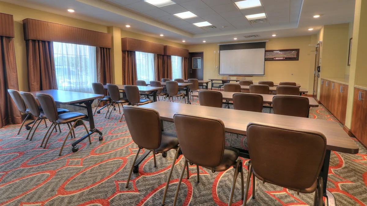This image showcases an interior meeting room equipped with tables, chairs, and a projector screen, set up for collaborative activities such as meetings, workshops, or trainings. The setup exudes a professional, productive atmosphere ideal for business travelers.