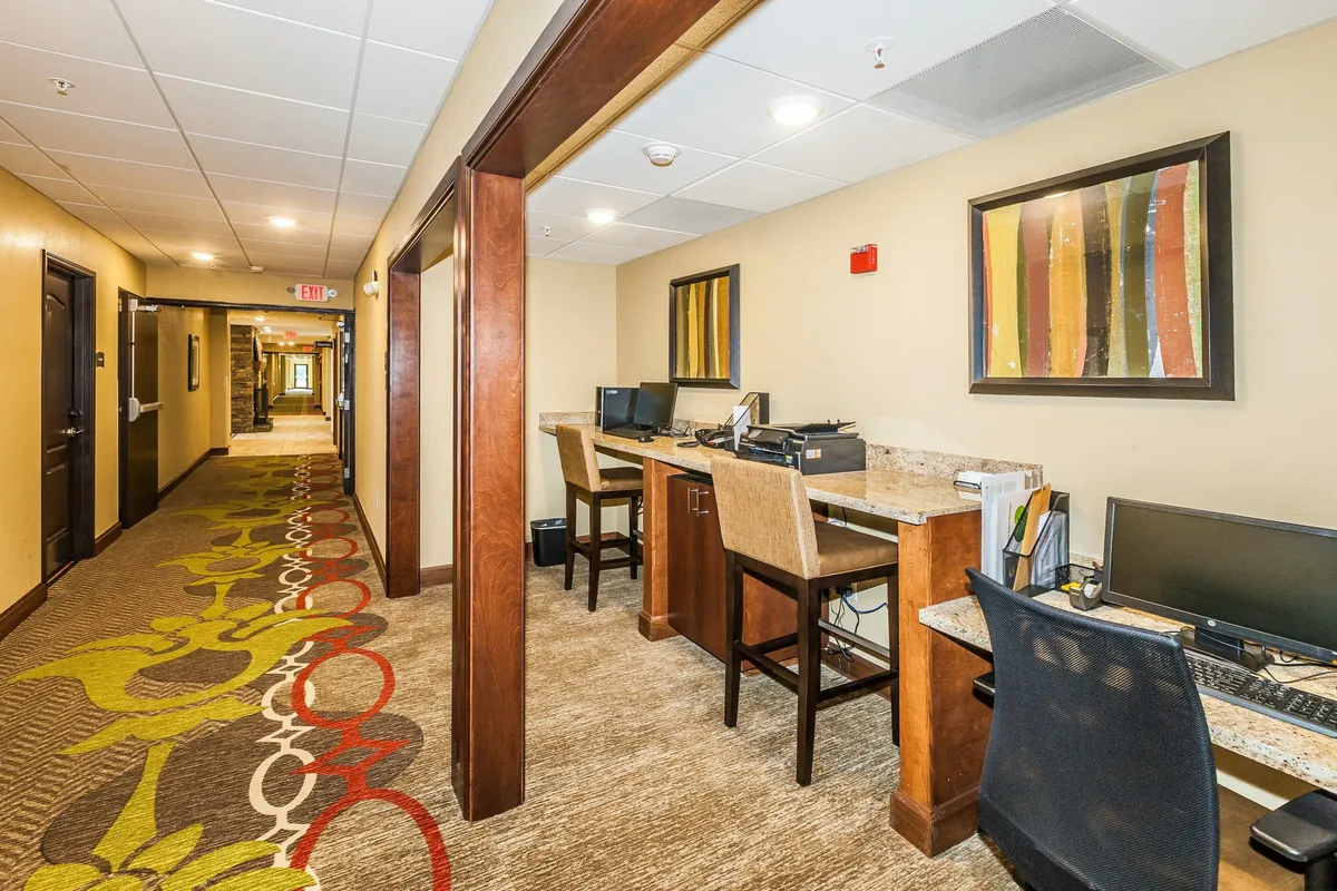 A contemporary business center interior, with computers, individual workstations, decorative artwork, and patterned carpeting. The space is designed for productivity, offering guests a comfortable environment to work or check email.