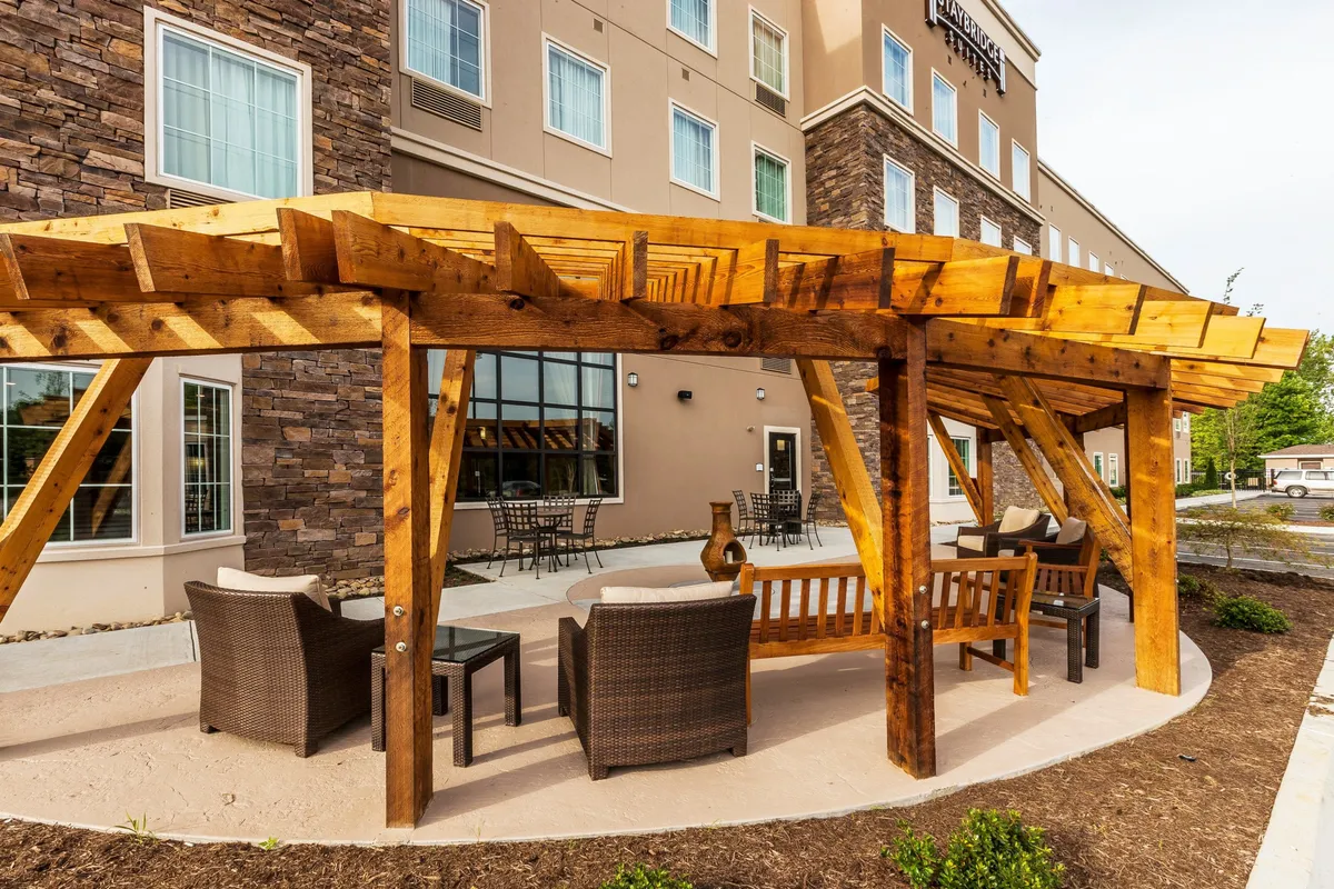This image features a cozy outdoor seating area beneath a wooden pergola adjacent to a stone wall. Comfortable chairs encourage relaxation, while the sunset view creates a warm, inviting mood. The space is ideal for unwinding after a day spent shopping or exploring the neighborhood.