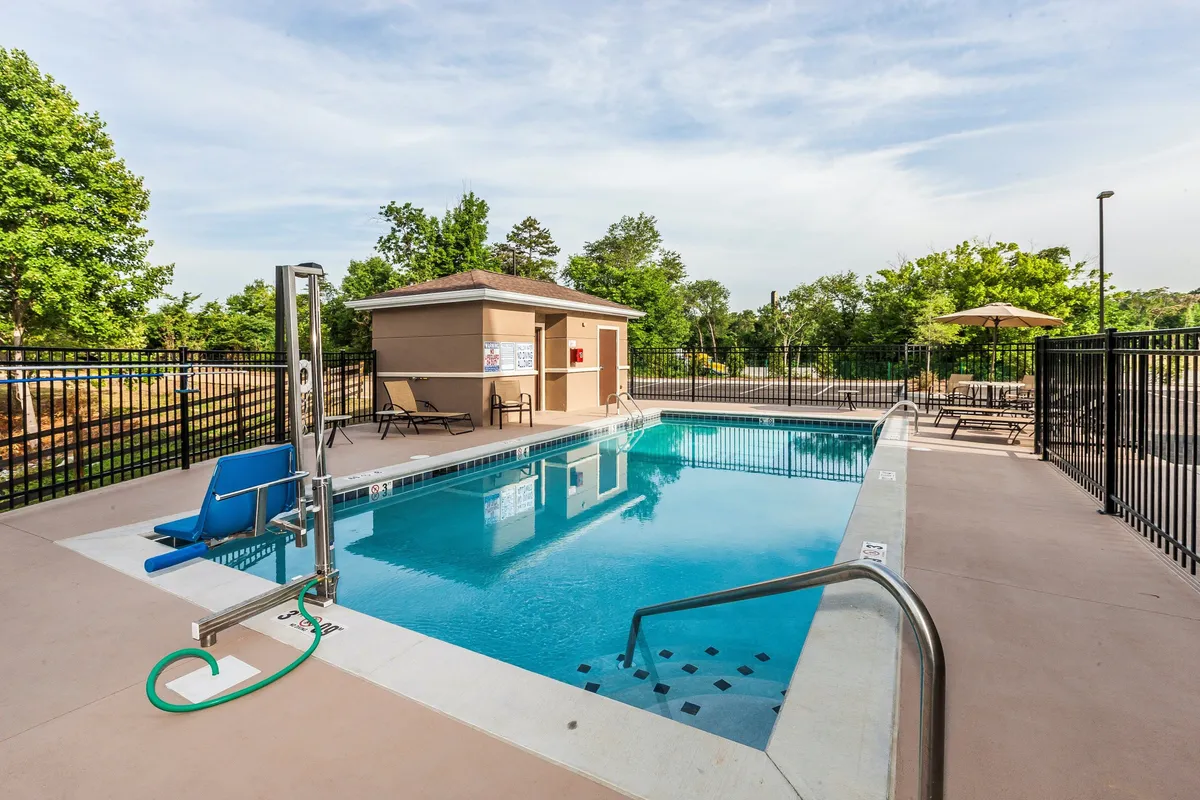 A vibrant exterior shot of the property's outdoor swimming pool, surrounded by poolside seating and an accessible lift. The area is bathed in sunset light, with guests enjoying a swim and relaxing on lounge chairs. The overall mood is cheerful and relaxed, inviting guests to enjoy summer leisure.